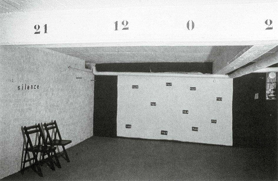 Ausstellungsansicht mit weißer, wandfüllender Filmleinwand, auf die die kleinen, schwarzen Rechtecke mit den figure-Bezeichnungen gemalt sind.
