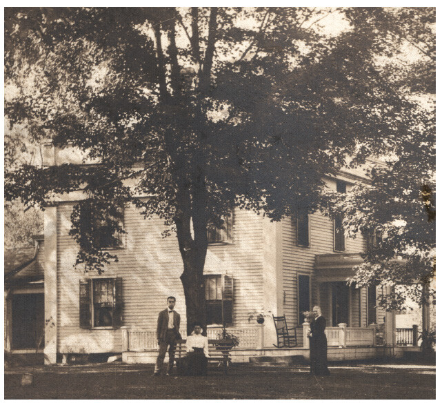 Small figures of Kang Tongbi seated, with Luo Chang at her side, Dr. Tudor on the right, beneath tall tree in yard of large white colonial house.