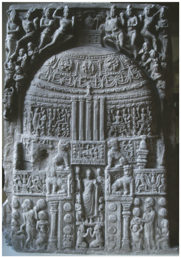 It depicts a miniature stūpa with intricate carving of narrative scenes. A standing Buddha with devotees is placed at its entrance. There are flying figures above the stūpa.