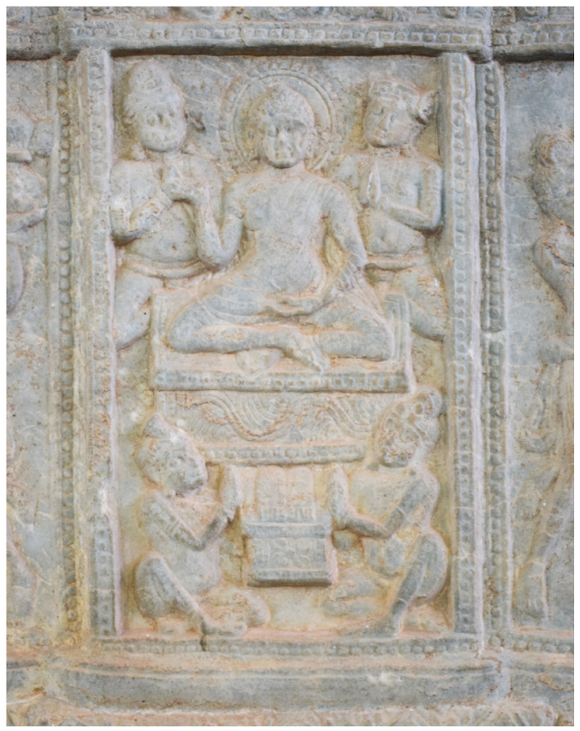 It shows a seated Buddha with four attendants depicted at the center of the base section of the miniature stūpa. A set of footprints is depicted in front of the Buddha.