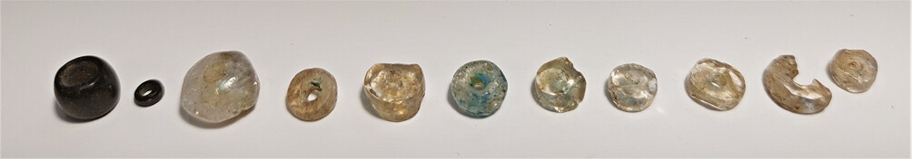 Various pierced beads (NAM P4707.1â11) from Shaft Grave I, made from transparent, sometimes light blue-green coloured minerals, some probably crystal. From left: the large black bead (no. 1) weighs 0.38 g, the little black bead (no. 2) weighs 0.04 g, the large white bead (no. 3) weighs 0.65 g, and the greenish-blue spotted bead (no. 6) weighs 0.25 g.